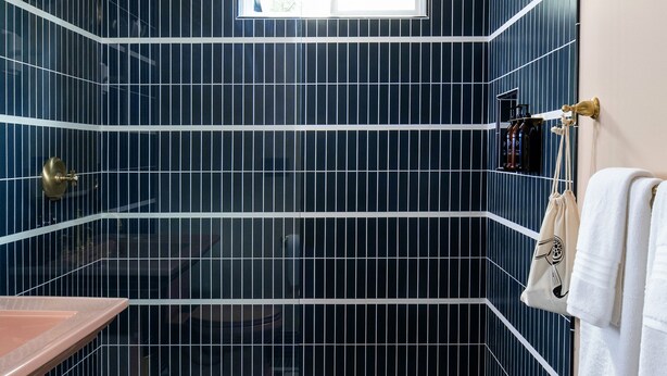Un baño con paredes de azulejos azul oscuro, suelo a cuadros blanco y negro, una ventana y un perchero con toallas.