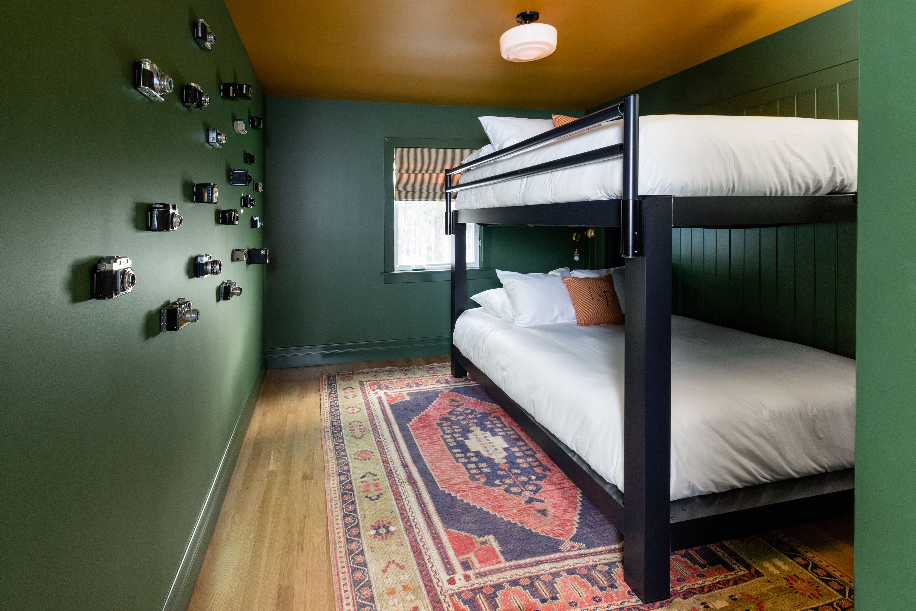 A bunk bed room with a green wall, a patterned rug, and a window with blinds.