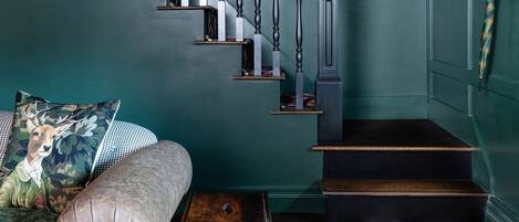 A staircase with a checkered floor, a sofa with a floral pillow, and a wall-mounted hat rack.