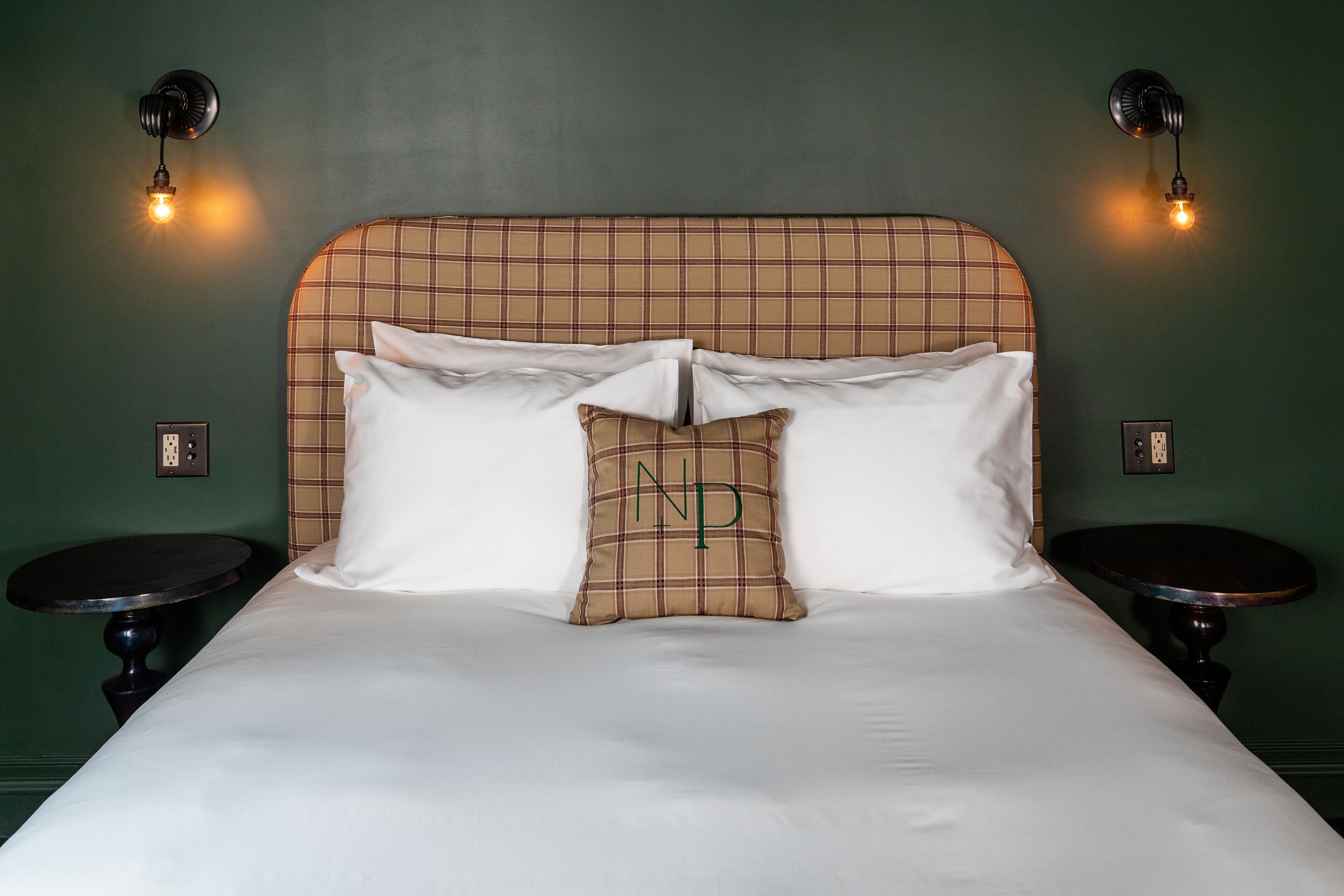 A neatly made bed with a plaid headboard, two bedside tables, and wall-mounted light fixtures.