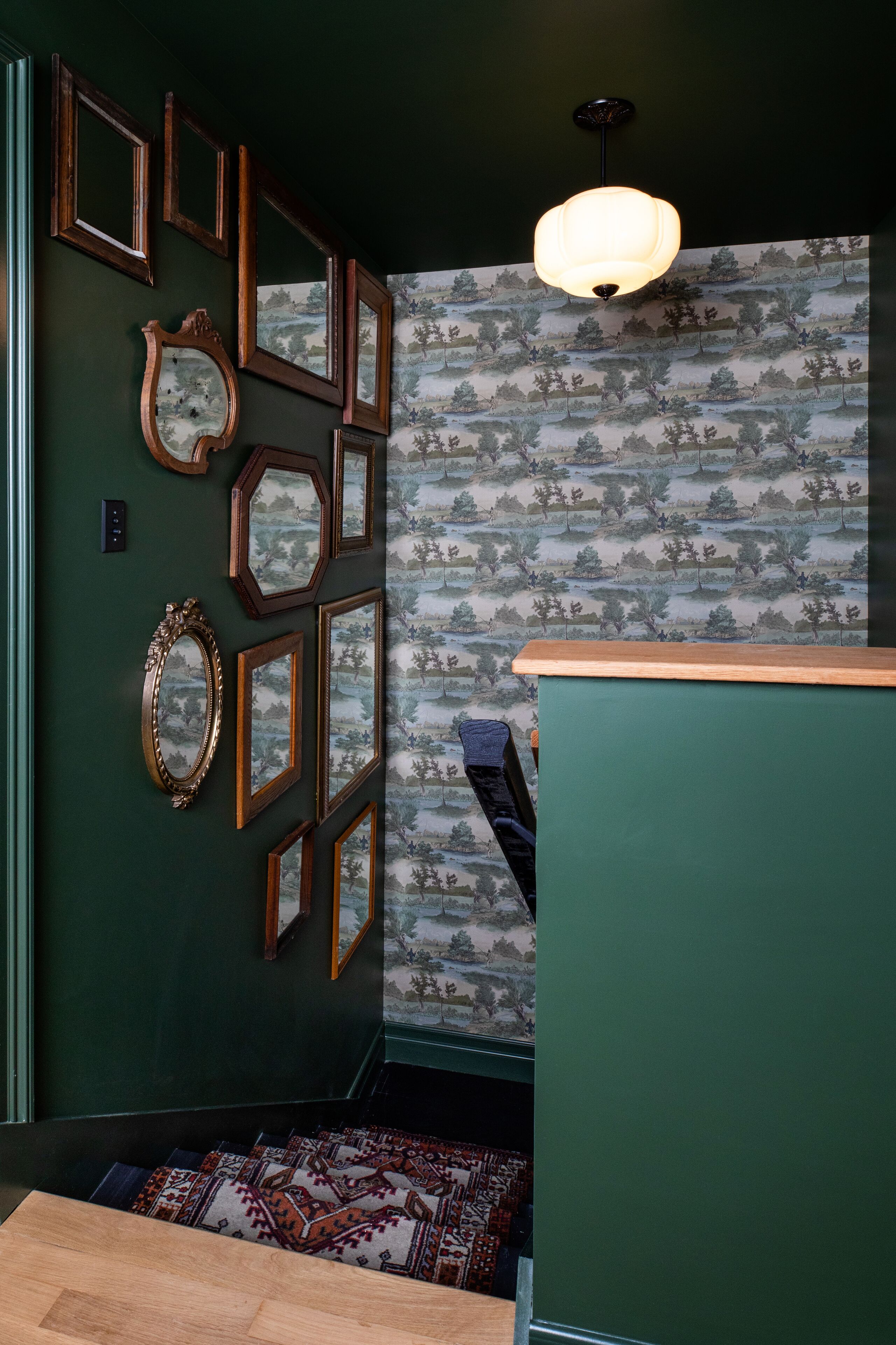 A room with a green wall, multiple framed mirrors, a patterned wallpaper, and a wooden bench.