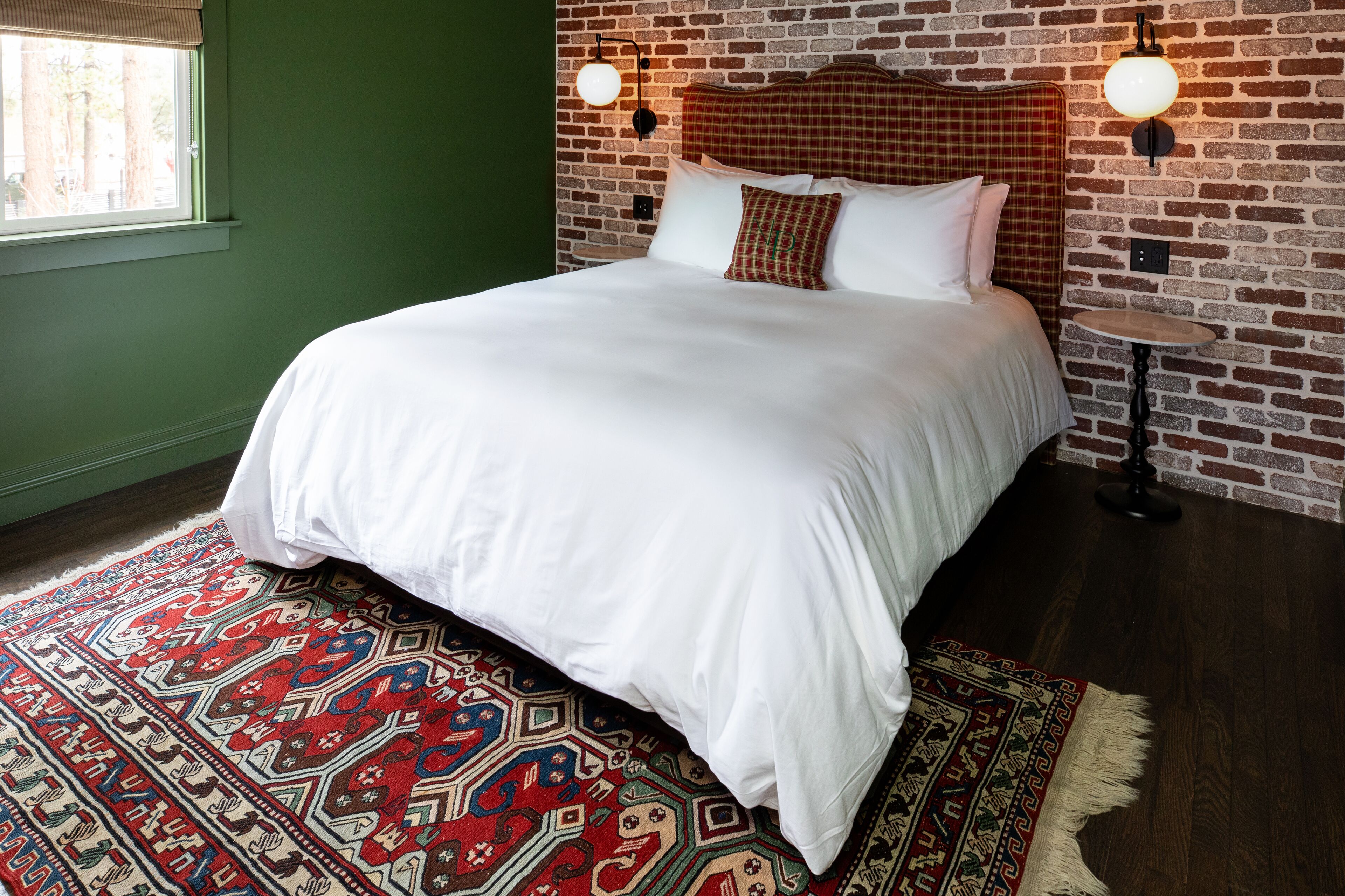 A neatly made bed with white linens, a patterned rug, and a brick wall with a headboard.