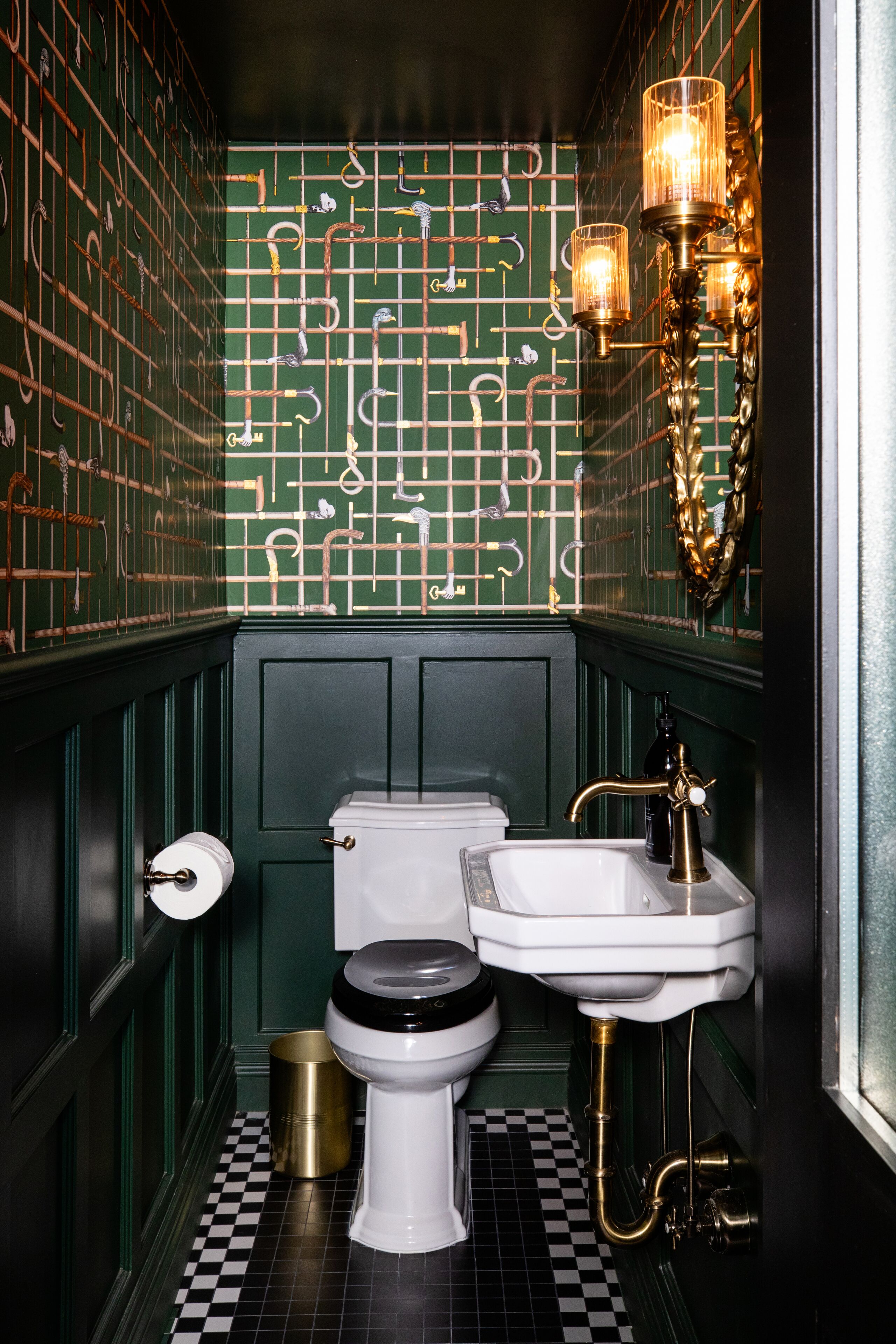 Ein Badezimmer mit Schachbrettboden, Toilette, Waschbecken und einer Wand mit grünem Gittermuster.