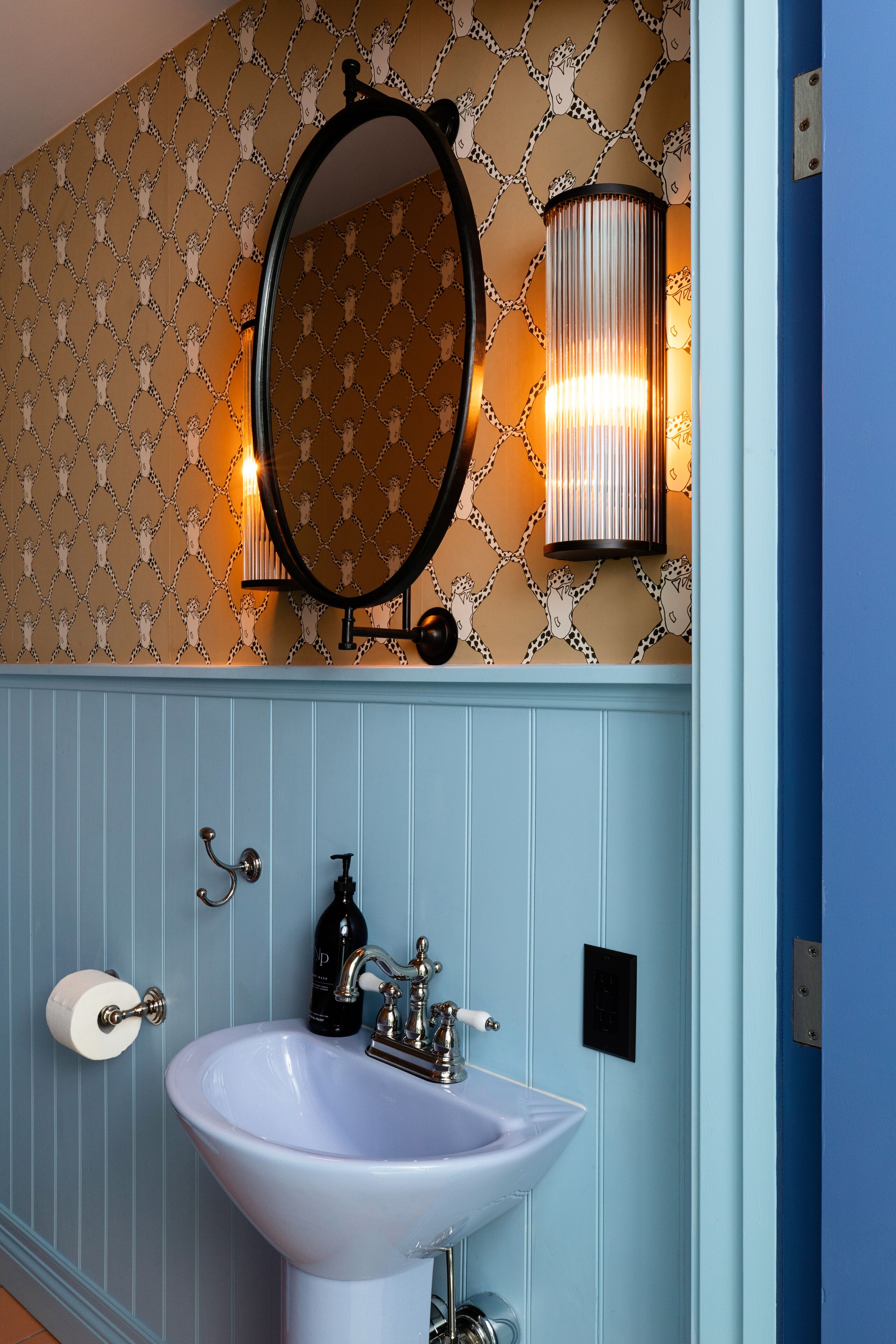 Une salle de bain avec un lavabo blanc, un miroir et un luminaire fixé au mur.