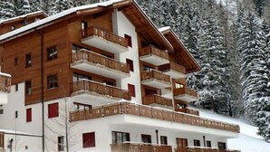 Et hotel med flere etager, træbalkoner og et snækt dækket bjerglandskab i baggrunden.