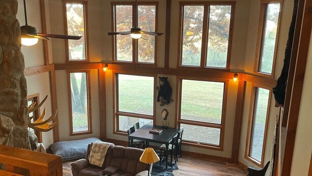 A spacious living area with a high ceiling, large windows, a dining table, and a cozy seating arrangement. - Cozy house nestled in the country (Linn)