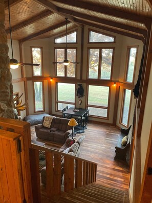 A spacious living area with a high ceiling, large windows, a dining table, and a cozy seating arrangement. - Cozy house nestled in the country (Linn)