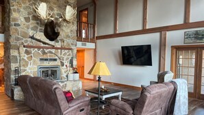 A cozy living room with stone walls, a fireplace, leather sofas, and a mounted deer head. - Cozy house nestled in the country (Linn)
