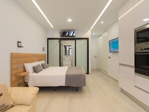 A modern hotel room with a wooden headboard bed, a flat-screen TV, a built-in oven, and a glass shower enclosure. - Cian Beach Home By CanariasGetaway (Las Palmas de Gran Canaria)