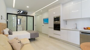 Ett modernt hotellrum med en säng, en soffa, en TV, ett litet kök och en skjutdörr till badrummet.
