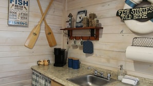 A kitchen with wooden walls, a sink, and various kitchen items like mugs and a coffee maker. - Fish Cabin at Mountain View Retreat (Talihina)