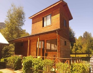 Cozy cabin with a gabled roof and a small porch area, featuring a window on the upper floor and a door on the lower level, surrounded by a fenced garden.