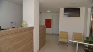 A reception area with a wooden reception desk, two beige chairs, a red door, and a potted plant. - Boa Esperança Apart Hotel (Boa Esperanca)