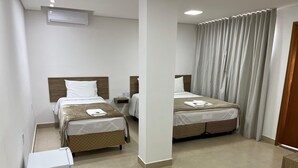 A hotel room with two beds, a small bedside table with a lamp, a built-in air conditioner, and a refrigerator. - Boa Esperança Apart Hotel (Boa Esperanca)