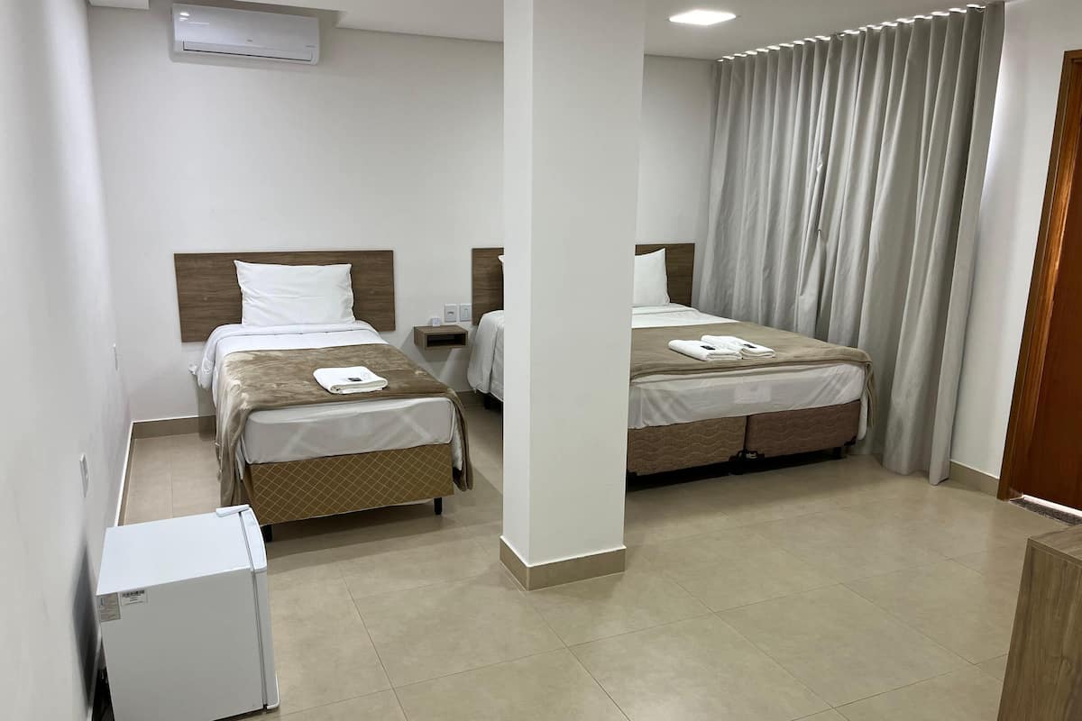 Habitación de hotel con dos camas, una mesita de noche con lámpara, aire acondicionado integrado y un refrigerador.