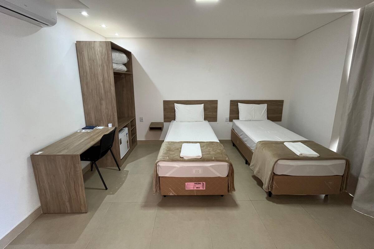 Habitación de hotel con tres camas individuales, un escritorio y un armario.