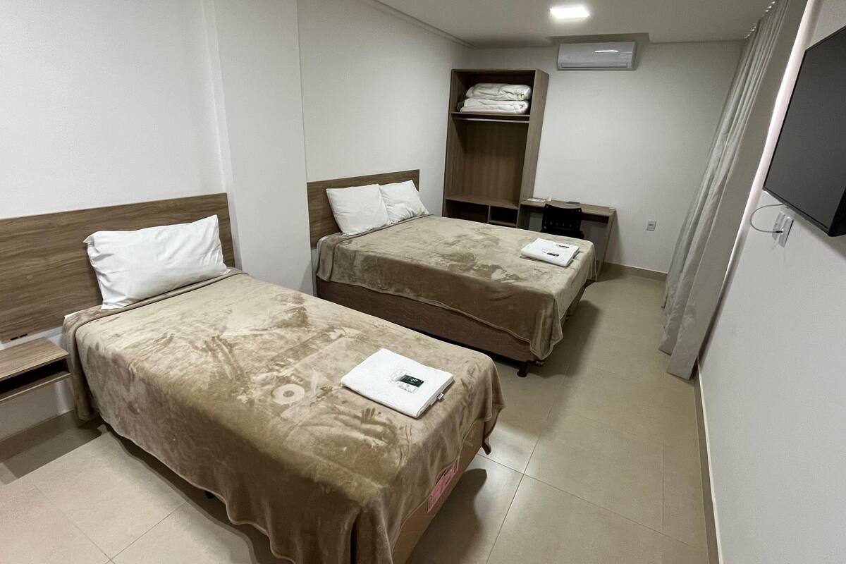 Habitación de hotel con dos camas, televisión, armario y escritorio.