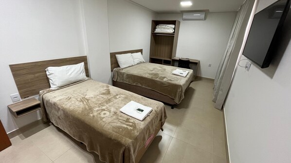 A hotel room with two beds, a TV, a wardrobe, and a desk.