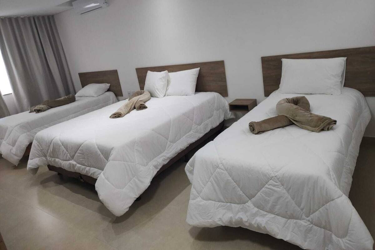 Habitación de hotel con tres camas individuales, cada una con edredón blanco y toalla enrollada.