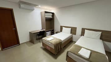 A hotel room with two beds, a desk, a wardrobe, and an air conditioning unit.