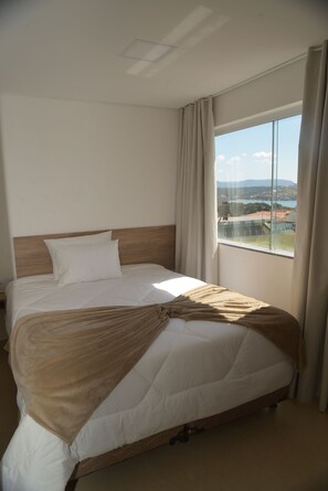 Habitación de hotel con una cama grande, cabecera de madera y vistas a la ciudad a través de un ventanal amplio.