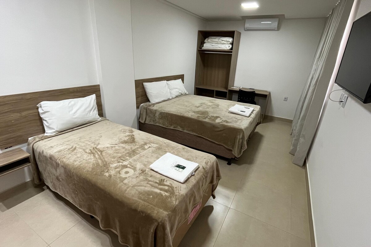 Habitación de hotel con dos camas, televisión, armario y escritorio.