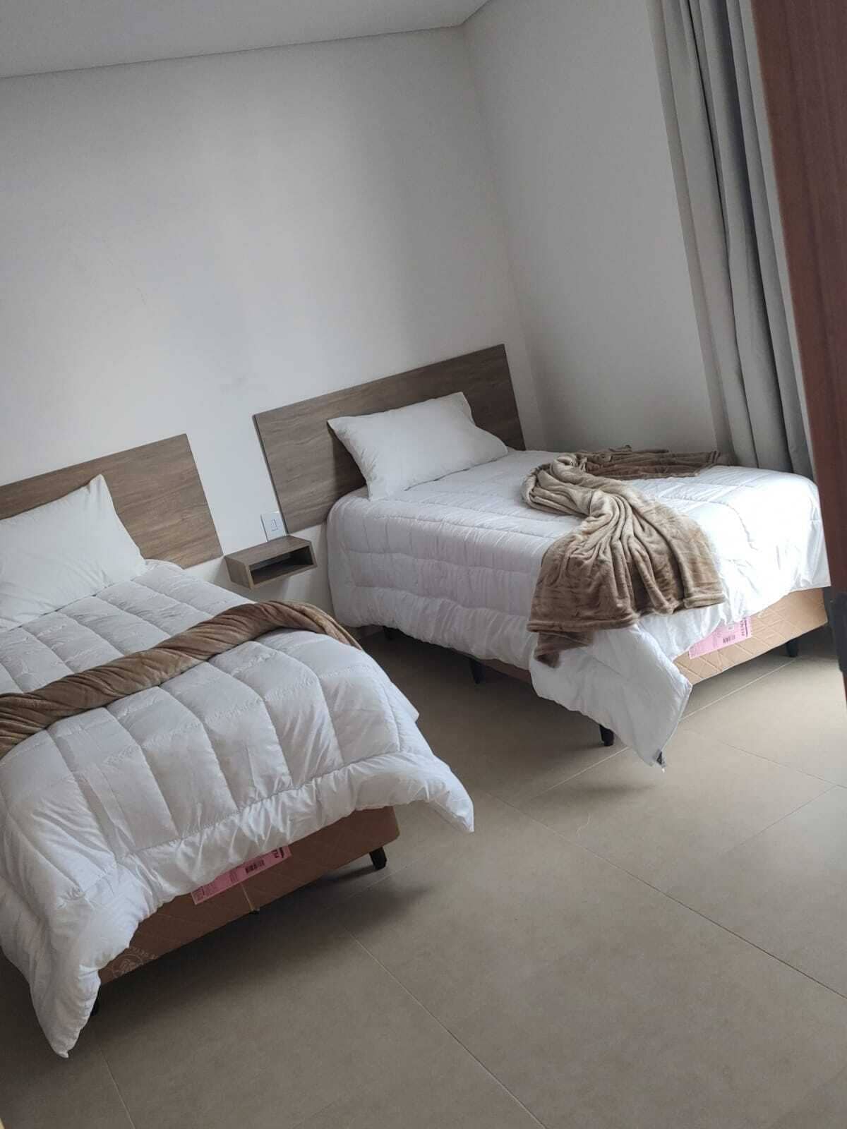 A hotel room with two beds, each with a wooden headboard, white bedding, and a brown throw blanket.