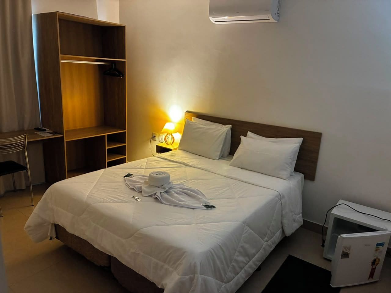 Una habitación de hotel con cama, mesita de noche, lámpara y armario.