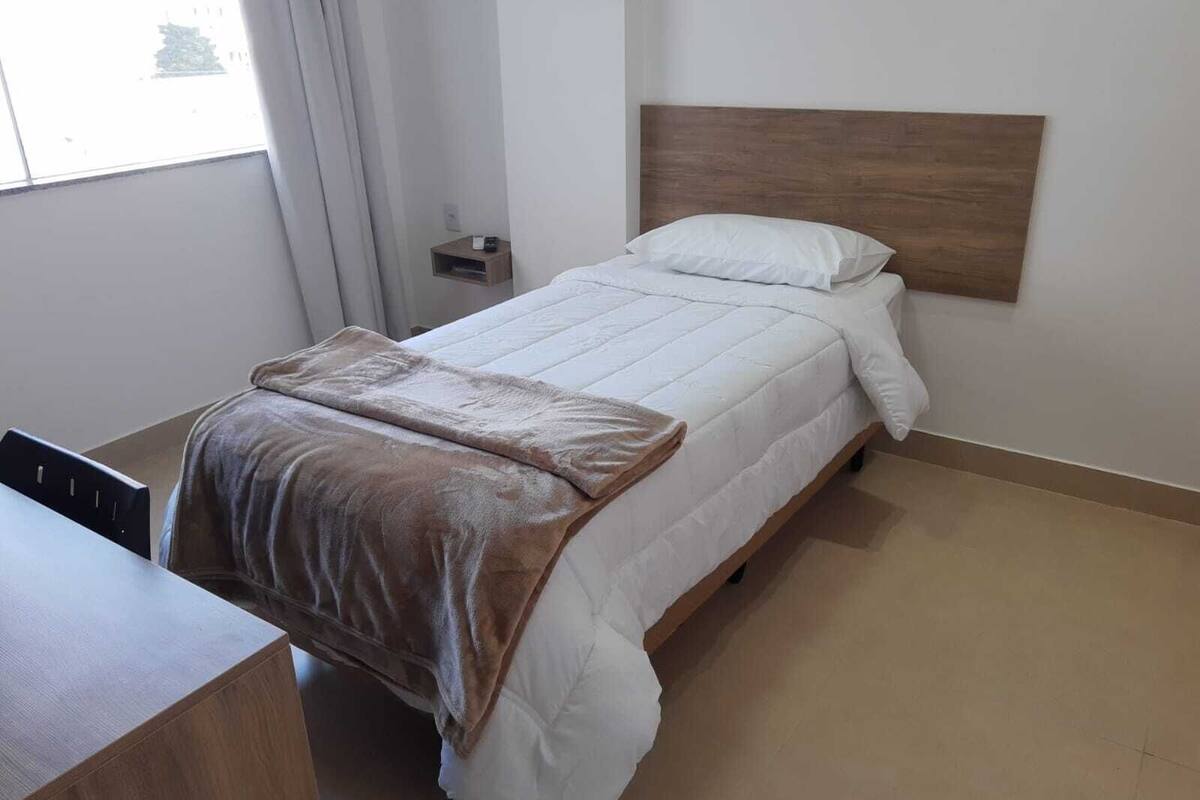 Una cama bien tendida con una manta marrón, un cabecero de madera y una mesita de noche con una lámpara.