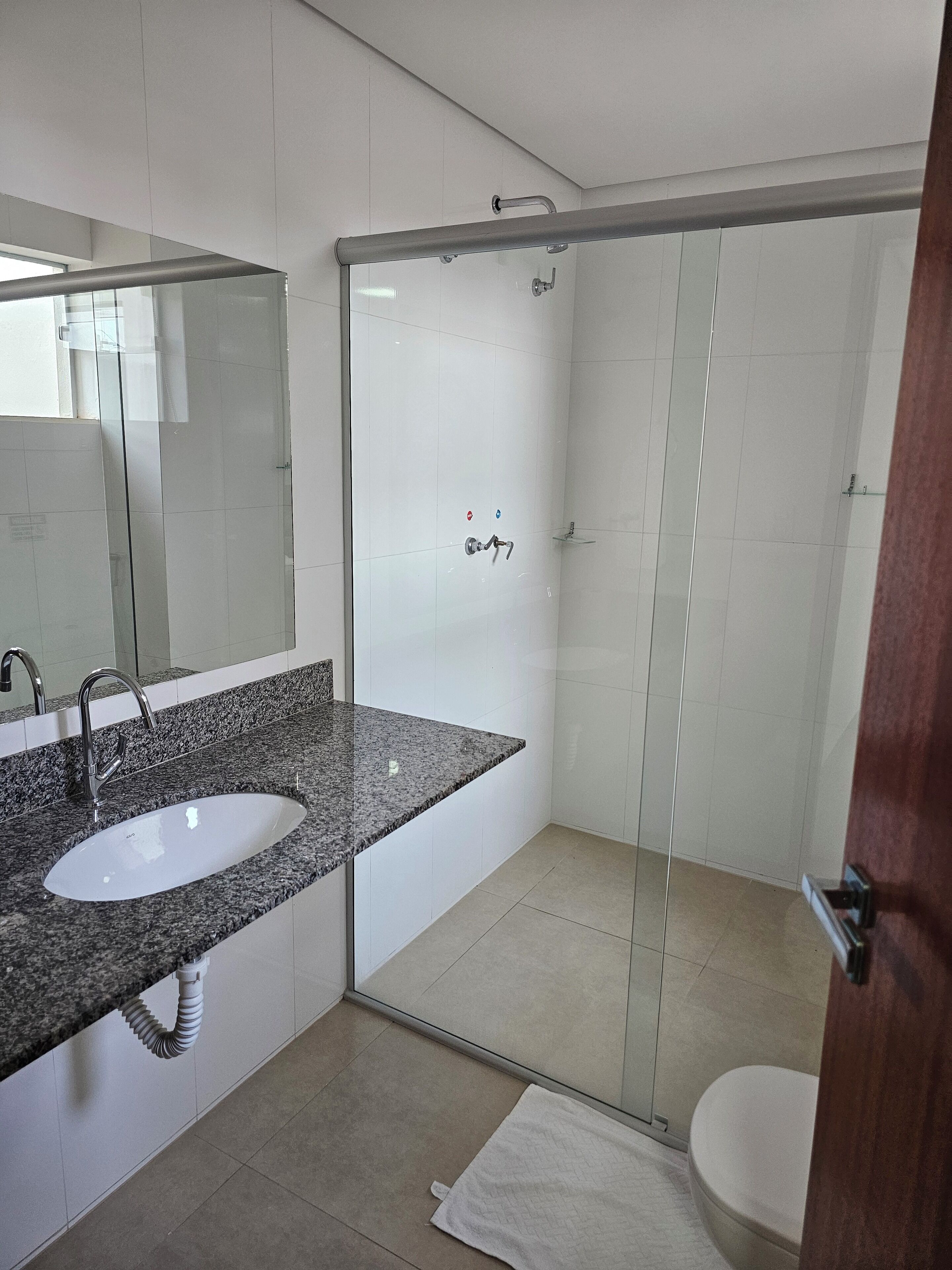 A modern bathroom with a granite countertop sink, a glass shower enclosure, and a toilet.