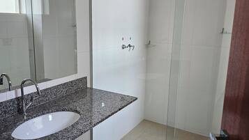 A modern bathroom with a granite countertop sink, a glass shower enclosure, and a toilet.