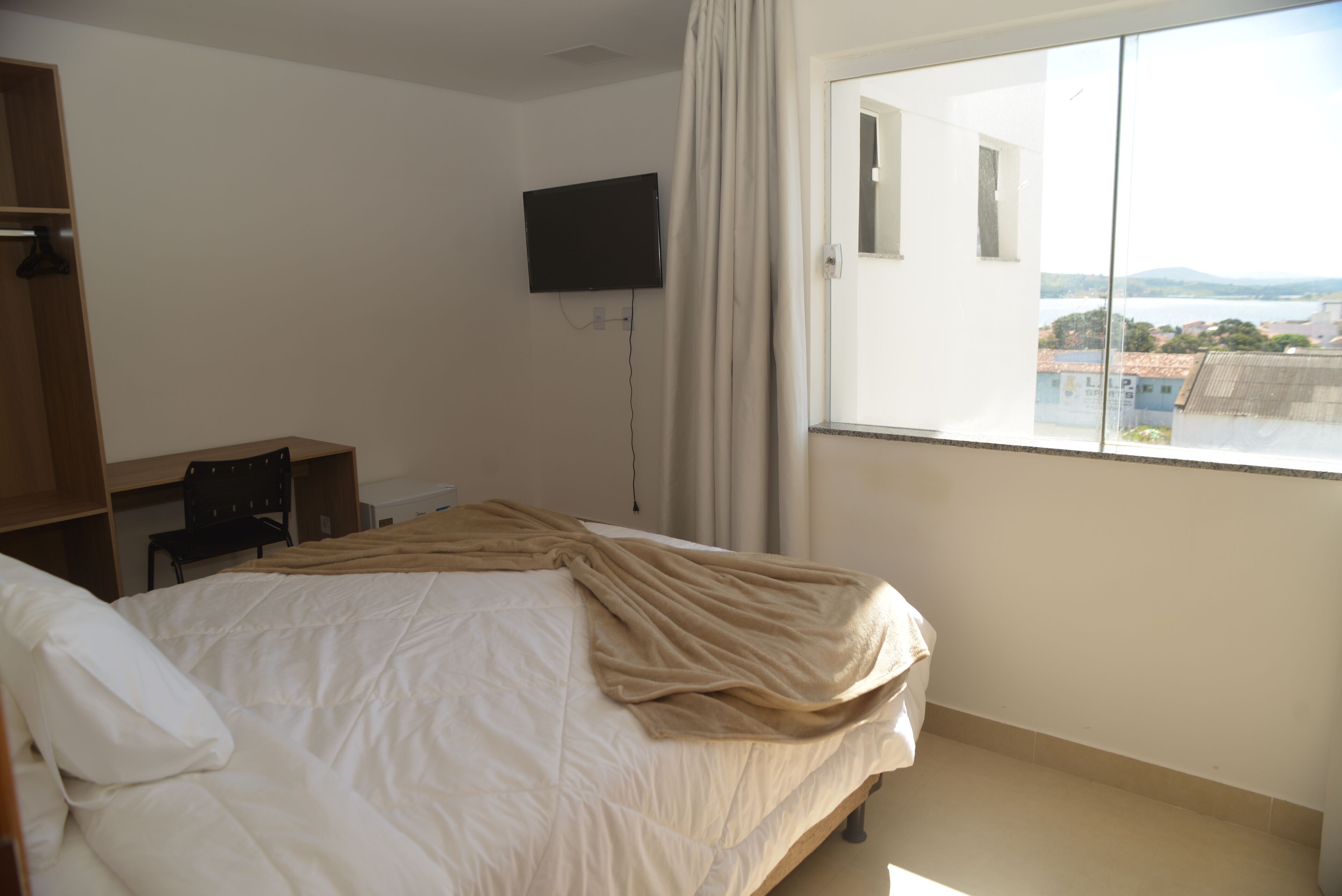 Ein Hotelzimmer mit Bett, Schreibtisch, Stuhl, Fernseher und Fenster mit Blick auf Gebäude und Berge.