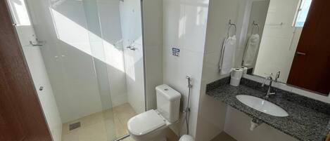 A modern bathroom with a glass-enclosed shower, a white toilet, a sink with a granite countertop, and a mirror above the sink.