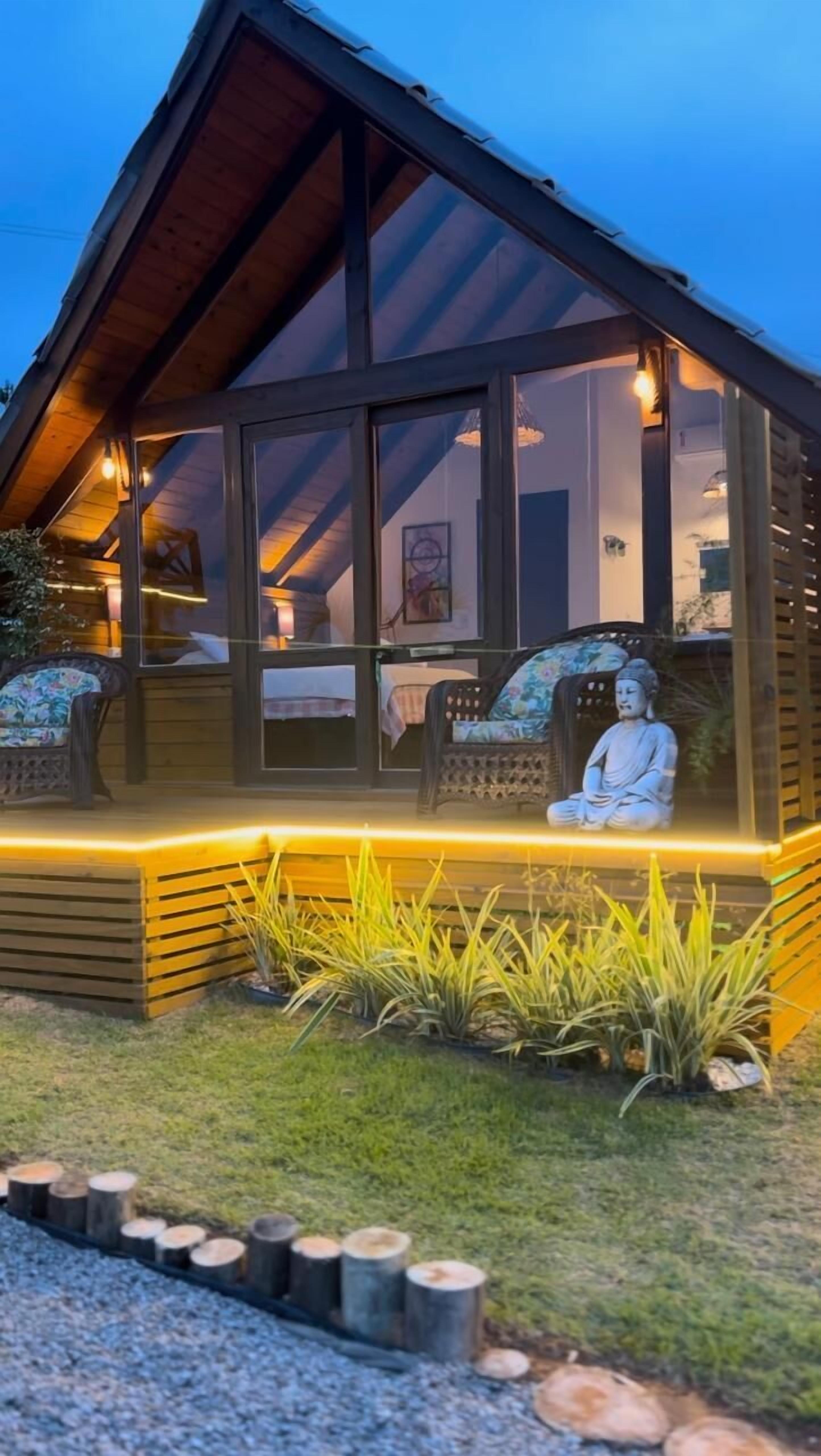 Een houten hutje met een glazen veranda, een Boeddhabeeld en een kleine tuin.