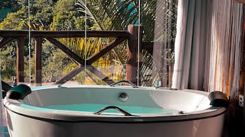 A hot tub with a wooden deck and a view of lush greenery.
