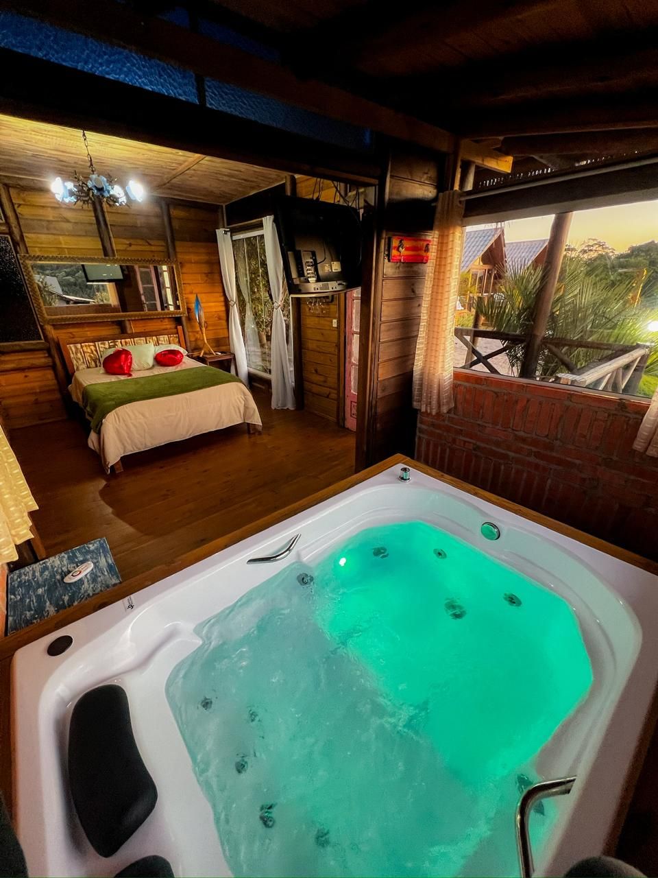 Ein Zimmer mit einer großen Badewanne, einem Bett mit roten Kissen, einem Fernseher und Blick ins Freie.
