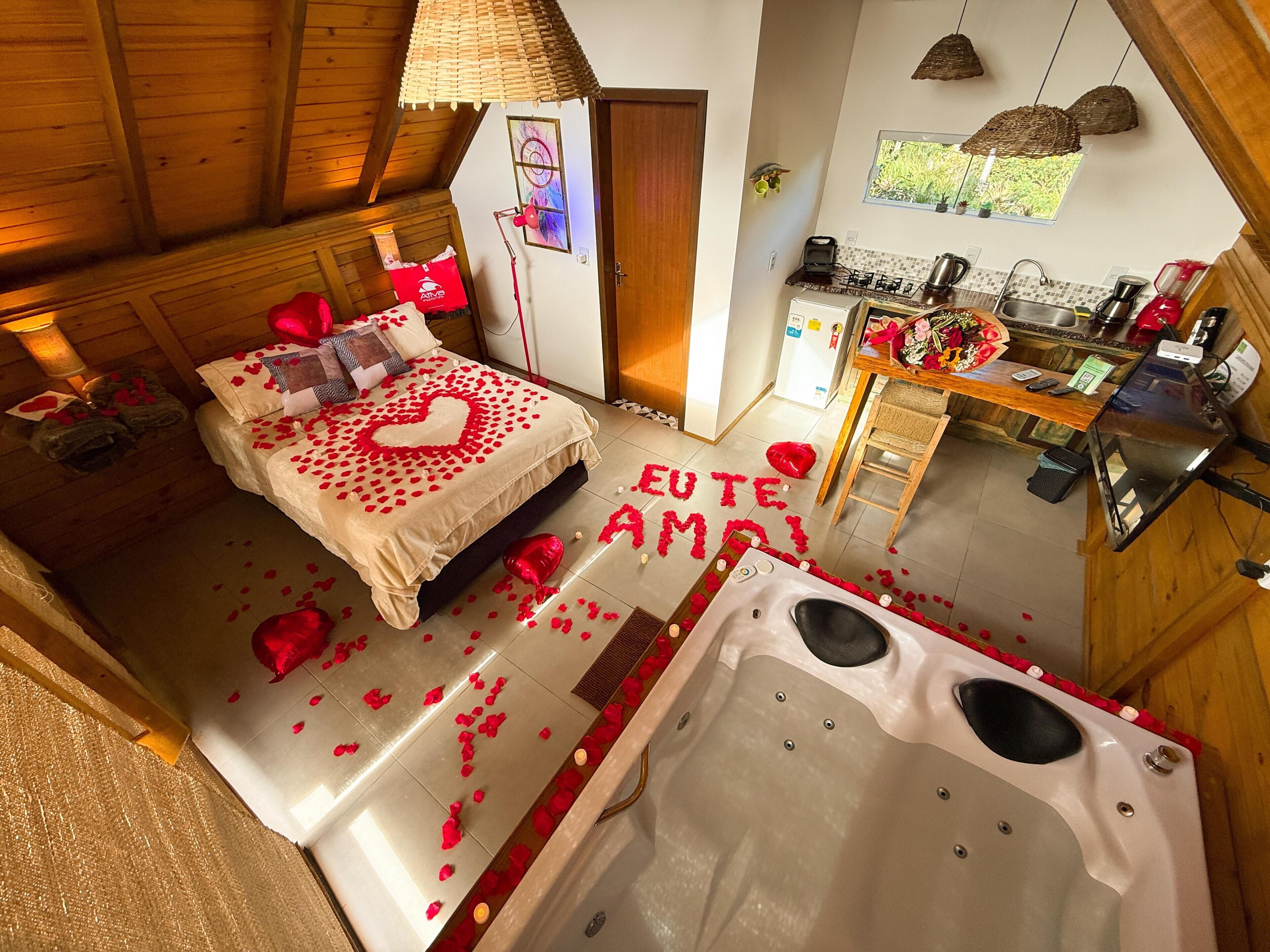 Ein gemütliches Zimmer mit einem Bett, das mit Rosenblättern und einer herzförmigen Anordnung geschmückt ist, einer Badewanne und einer kleinen Küchenzeile.