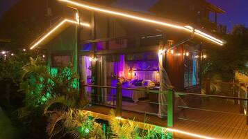 Uma casa moderna com varanda envidraçada, deck de madeira e interior aconchegante, com cama e área de estar.