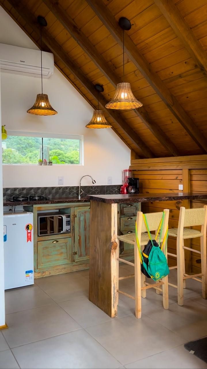 A rustic kitchen with wooden beams, a central island, and a view of greenery outside.