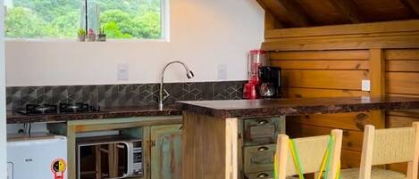 A rustic kitchen with wooden beams, a central island, and a view of greenery outside.