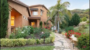 A house with a stone pathway leading to the entrance, surrounded by lush greenery and flowering plants. - Italian Estate in Wine Country (Temecula)