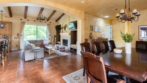 A spacious living room with a fireplace, a dining area with a large table and chairs, and a kitchen with wooden cabinets. - Italian Estate in Wine Country (Temecula)