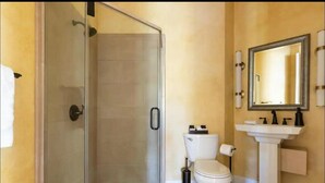 A bathroom with a glass shower enclosure, a toilet, a sink with a mirror above it, and a towel hanging on the wall. - Italian Estate in Wine Country (Temecula)