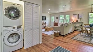 A laundry room with a front-loading washing machine and dryer, a wooden floor, and a cozy living area with a sofa and a dining table. - Highlands Escape, 1 mile to town - Retreat to the Mountains to Relax (Highlands)