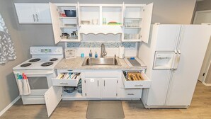 A compact kitchen with white cabinetry, a built-in stove, a refrigerator, and a countertop with various items.