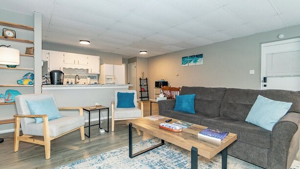 A modern living room with a grey sofa, two armchairs, a coffee table, and a kitchen in the background.