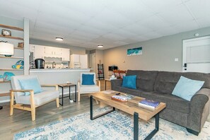A modern living room with a grey sofa, two armchairs, a coffee table, and a kitchen in the background. - Welcome to the High Street Suite (Fairport Harbor)