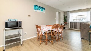 A dining area with a table, chairs, a microwave on a cart, and a view through a window.