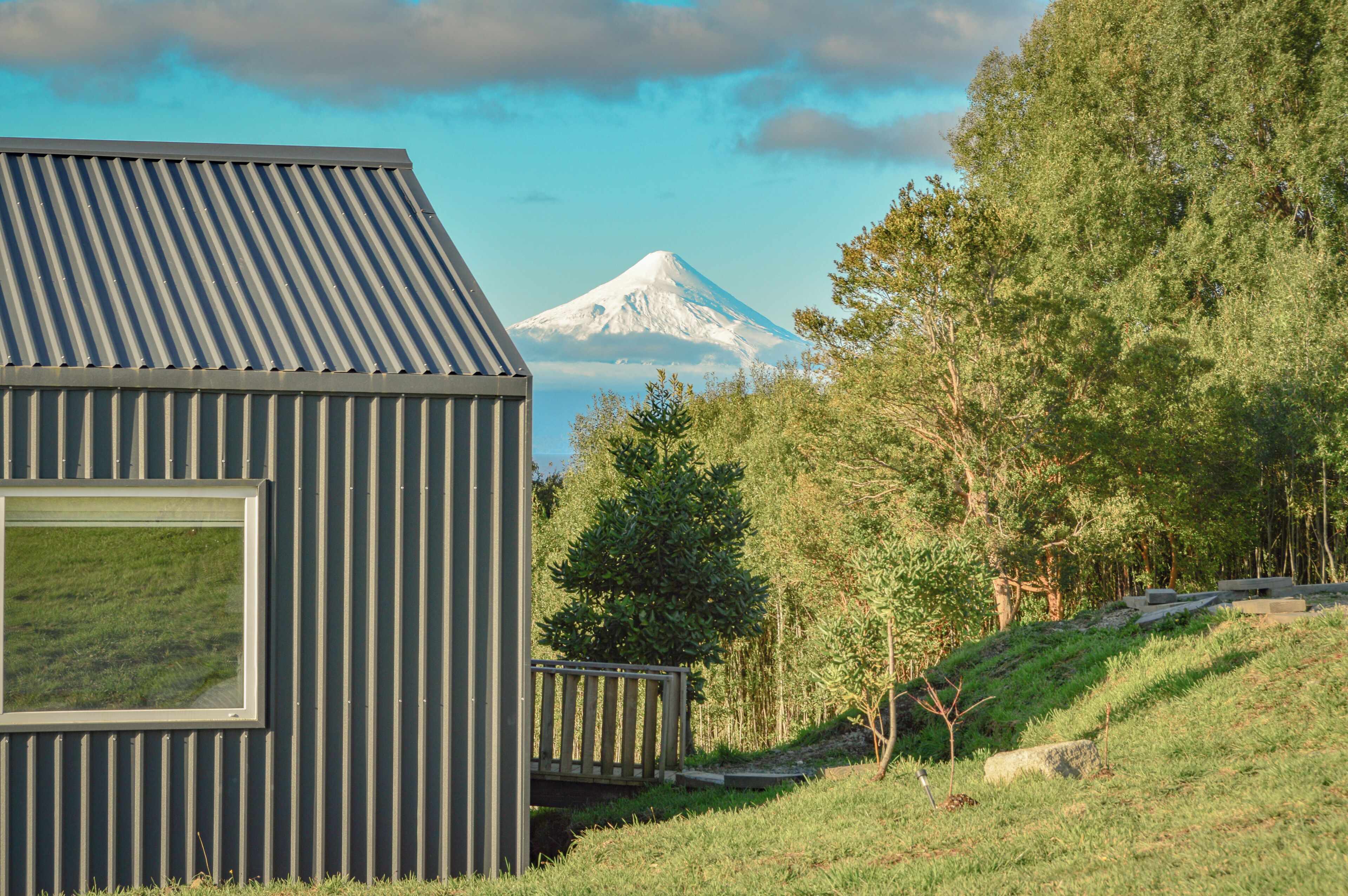 A modern building with a metal roof, a window, and a view of a snow-capped mountain.