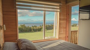 Un dormitorio con un ventanal que ofrece vistas a un campo cubierto de hierba y una montaña distante.